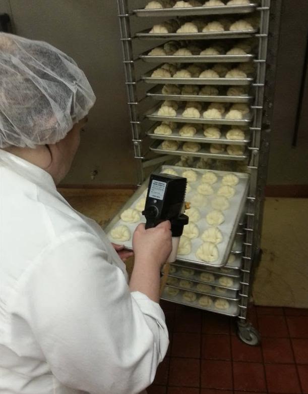Baker spraying trays of buns with egg wash on a bakery rack