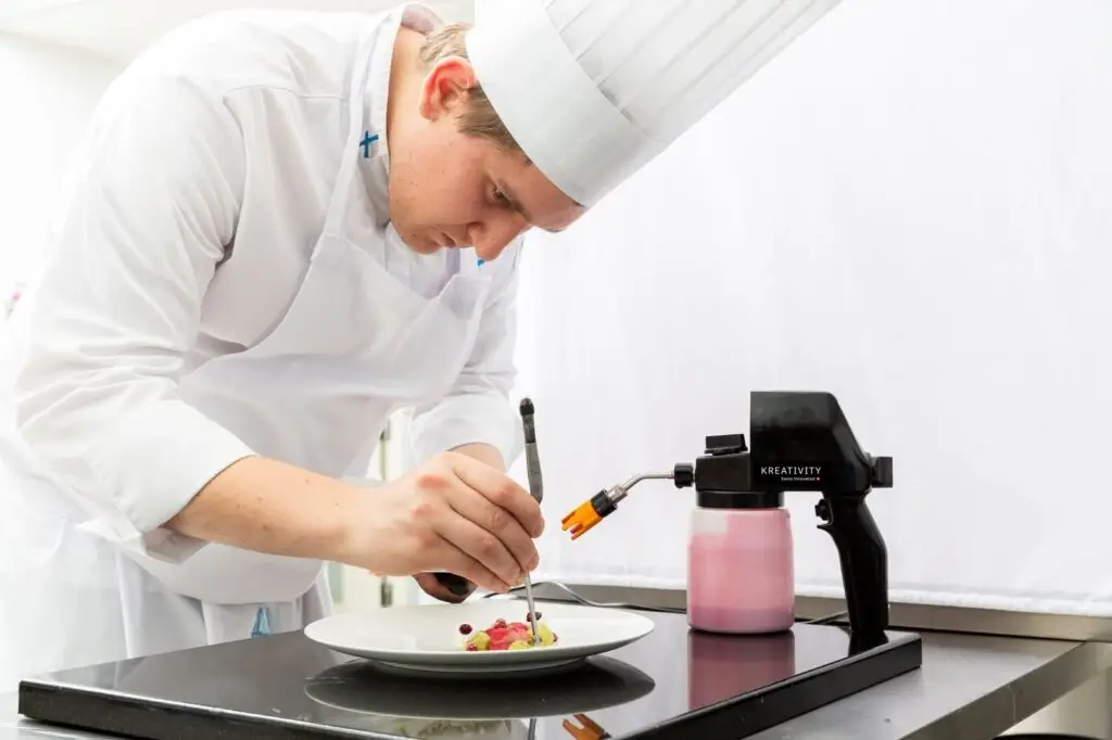 Chef plating a dish with a KREA Swiss sprayer on the counter